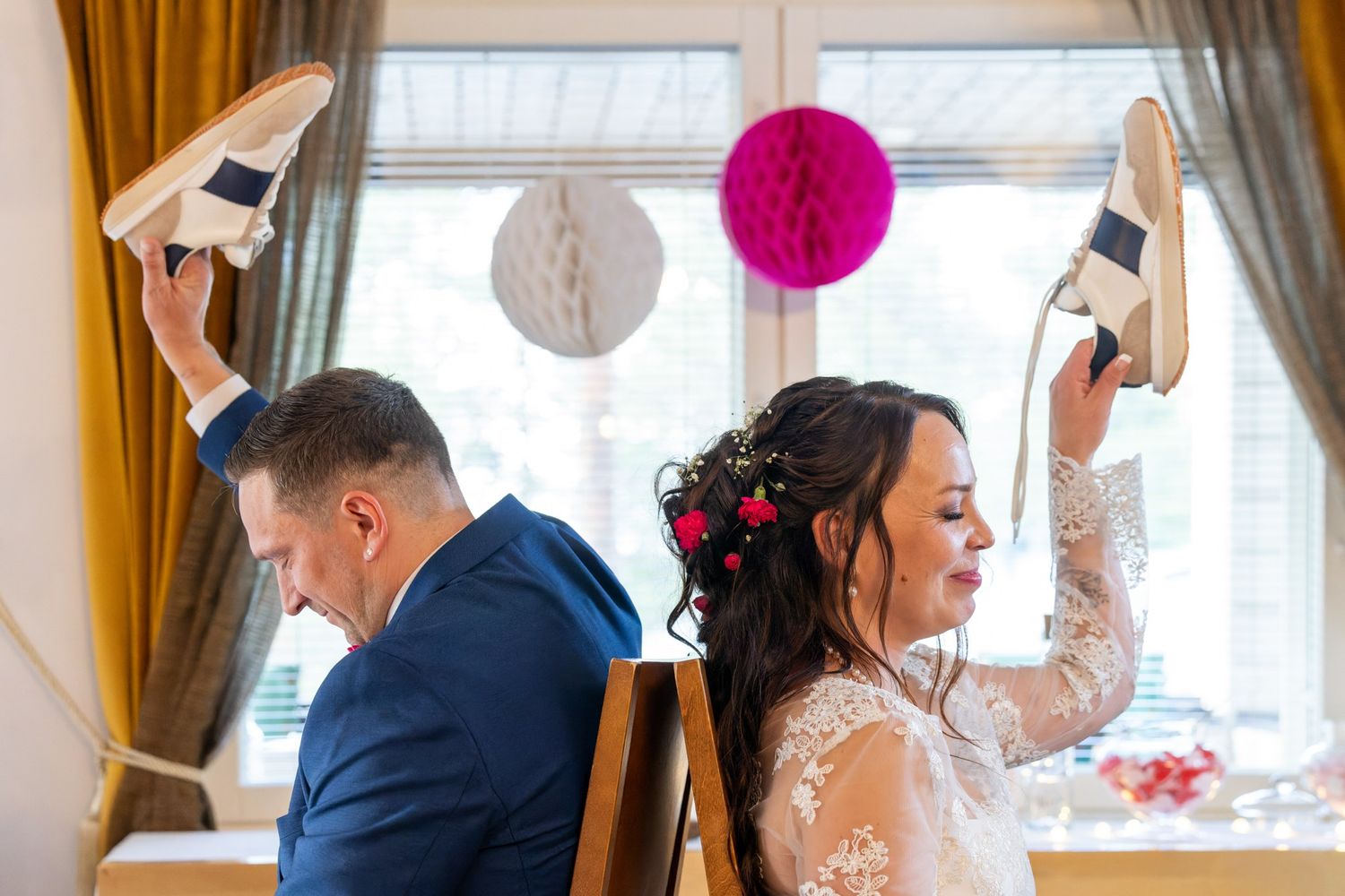 Couple celebrating at wedding reception while holding up their shoes in a playful moment.