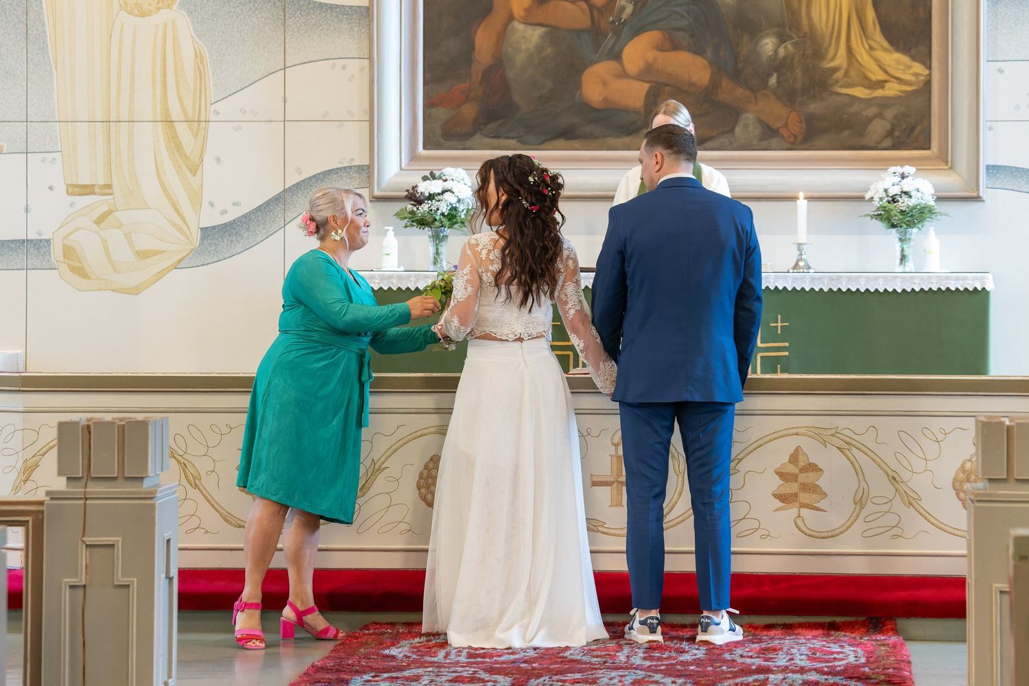 Wedding ceremony taking place in an elegant church interior with white and green floral decorations.
