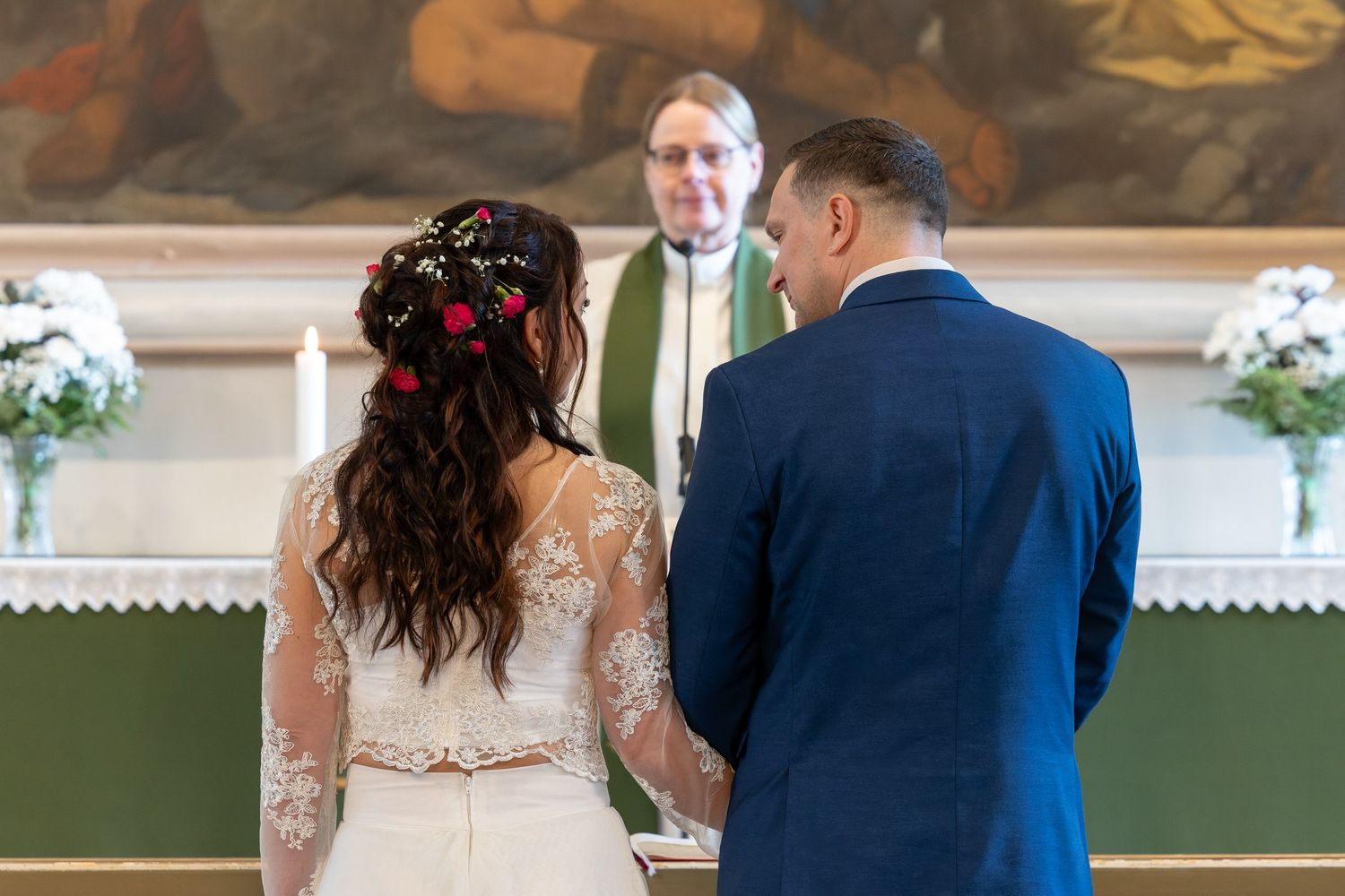 A couple stands at the altar with a priest in green robes during a church wedding ceremony.