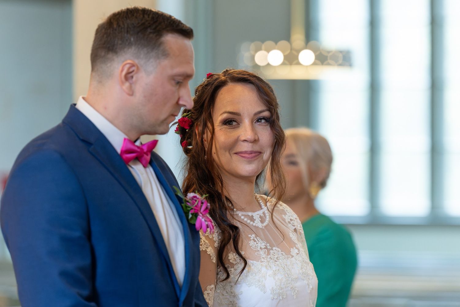 Wedding guests and bridal party members gather in a bright, modern venue with large windows.