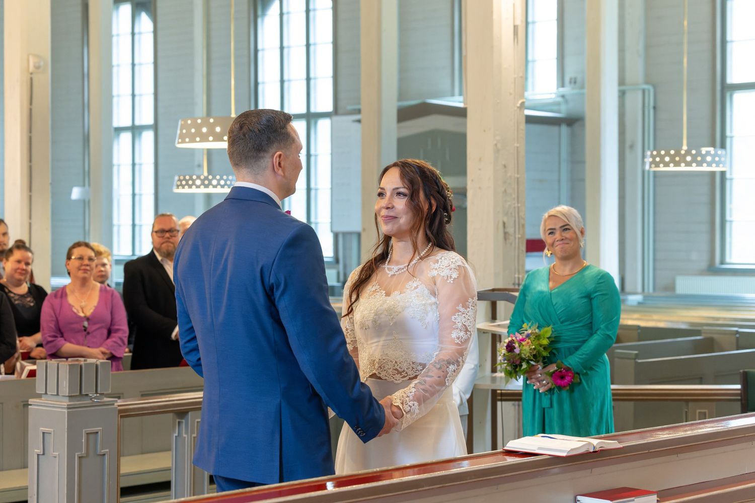 Wedding ceremony in a bright church sanctuary with guests seated in wooden pews and natural light streaming through windows.