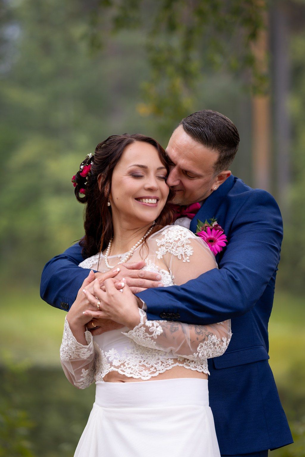 A couple shares an intimate dance moment in a forest setting, with the bride in lace and groom in navy blue suit.