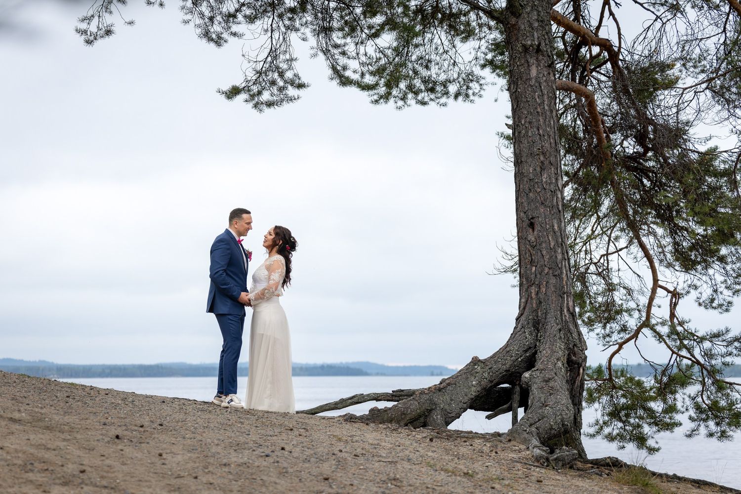 A couple in wedding attire stands together on a scenic cliff overlooking a misty mountain landscape.