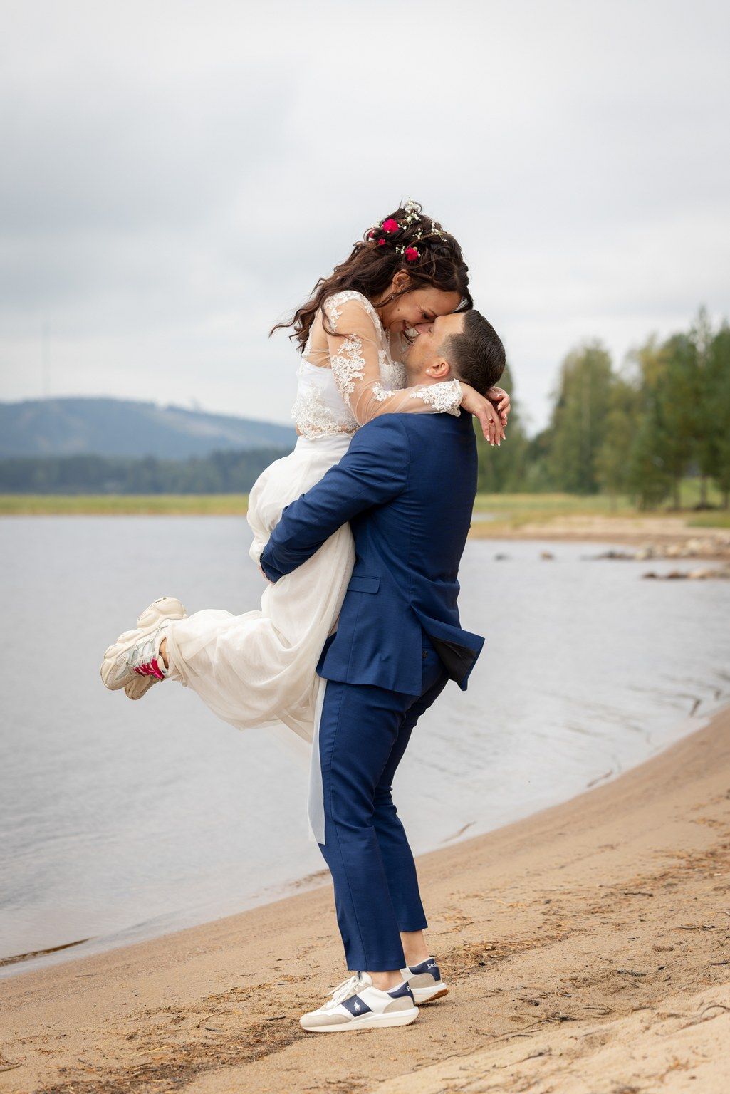 Couple embracing on beach shore with lake and mountains in background.