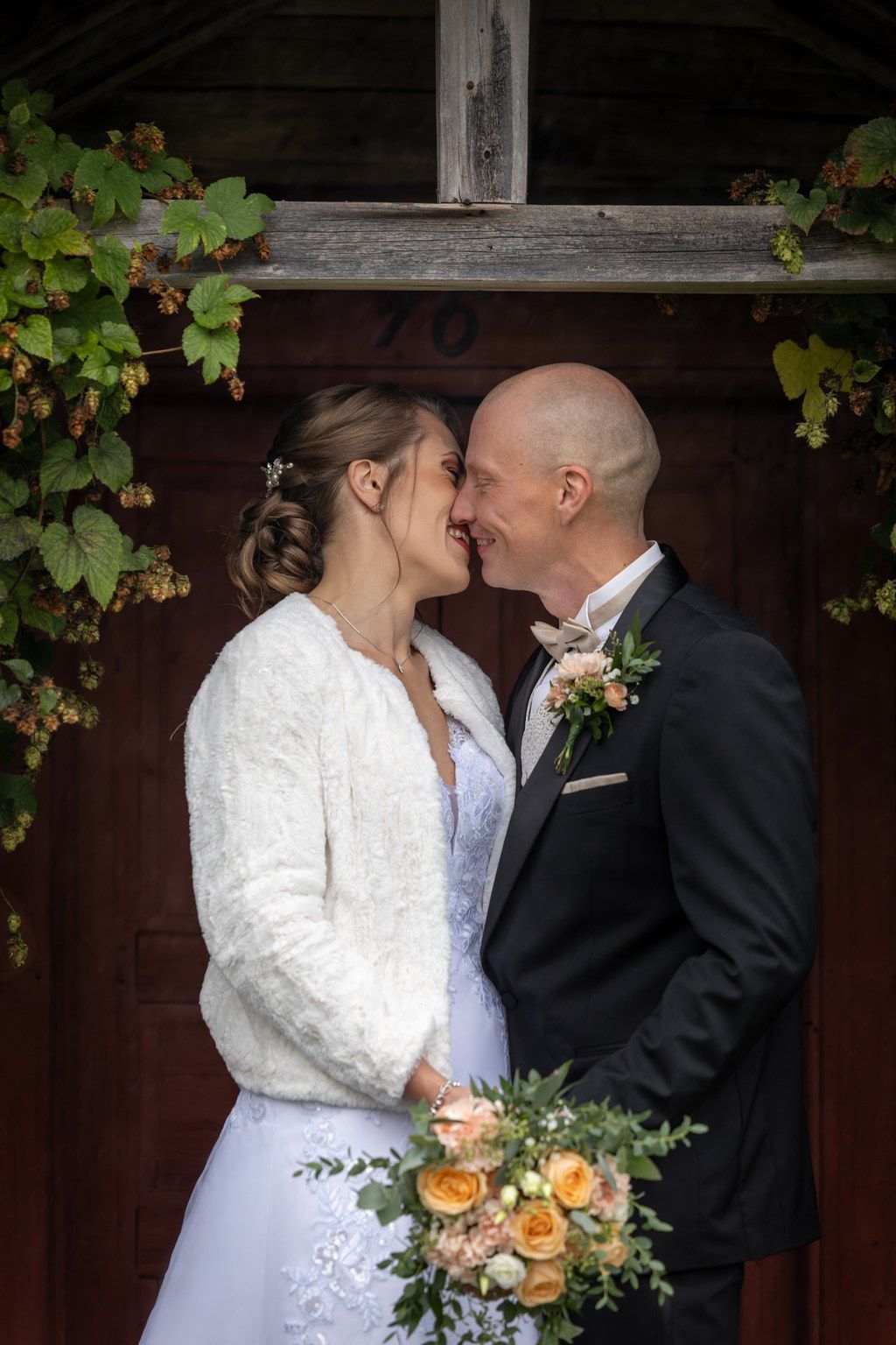 A couple in wedding attire share an intimate moment in front of a rustic wooden door with climbing vines.