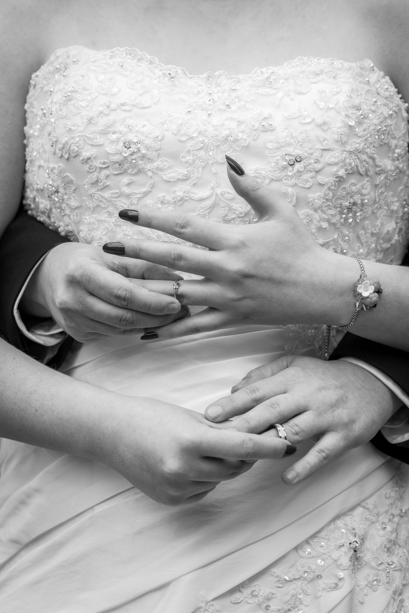 Black and white photo of newlyweds hands showing wedding rings, bride in lace dress with bracelet and dark nails.