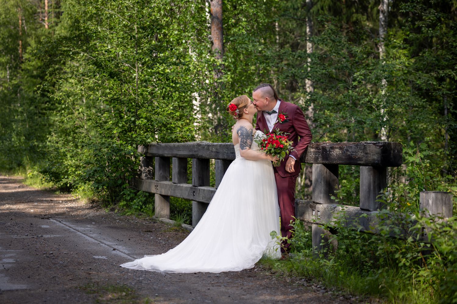 A romantic wedding couple embraces in a lush forest setting with natural greenery and sunlight filtering through trees.