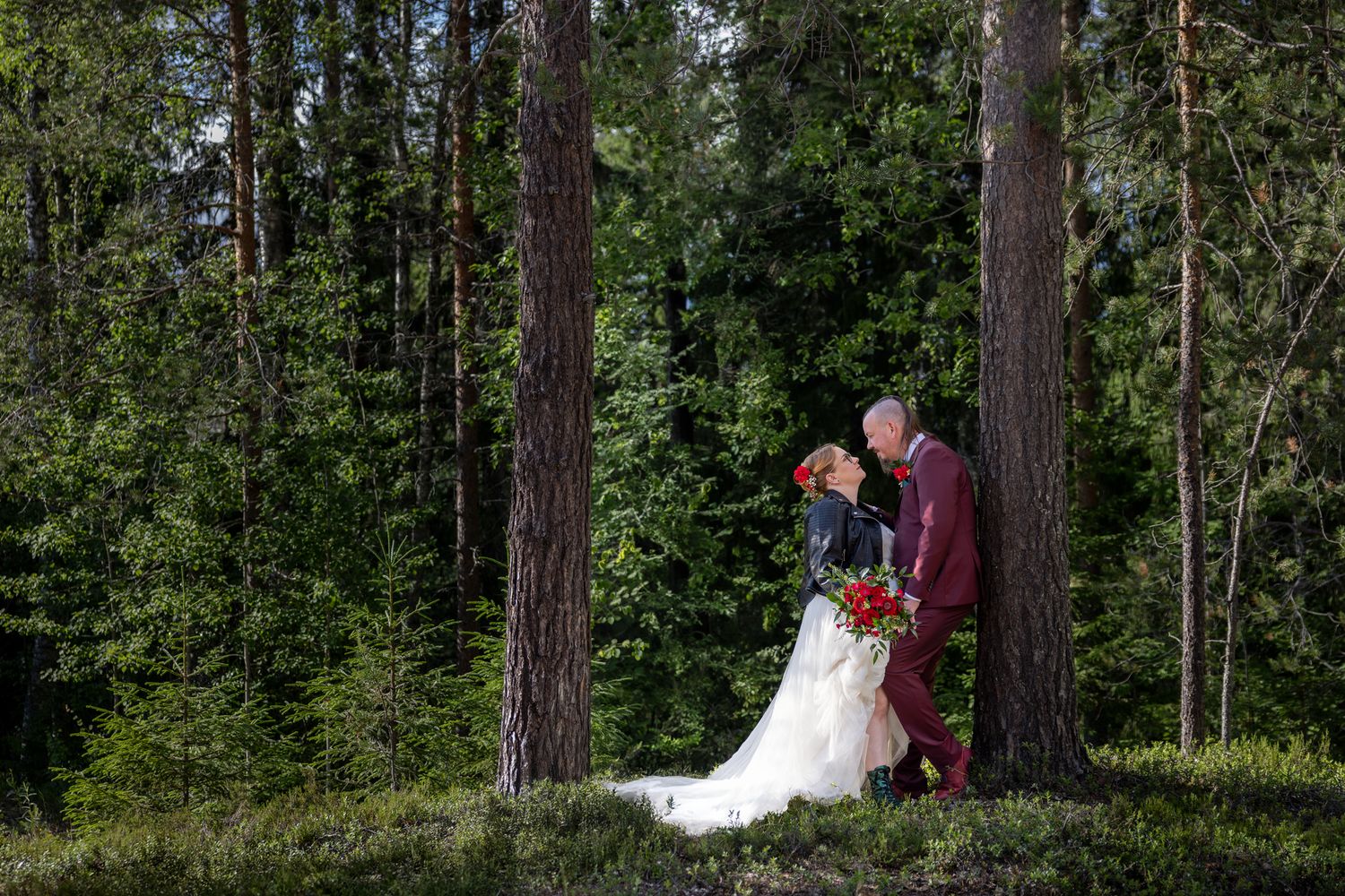 Couple in wedding attire poses in a lush forest setting with tall pine trees creating a romantic natural backdrop.
