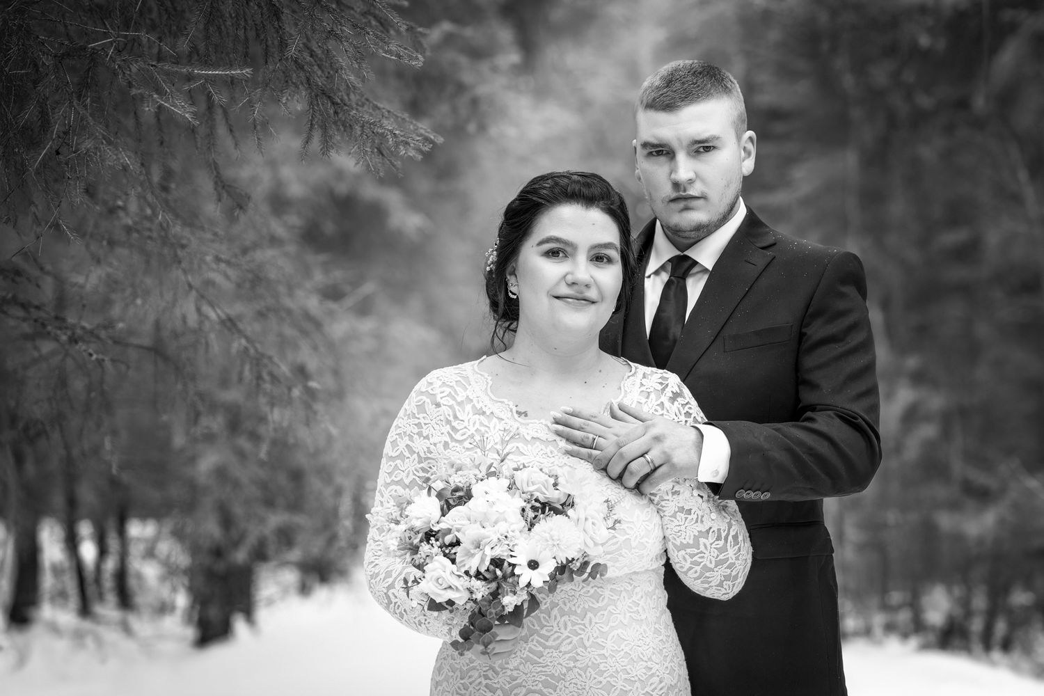 Mustavalkoinen kuva hääparista talvisessa metsässä.