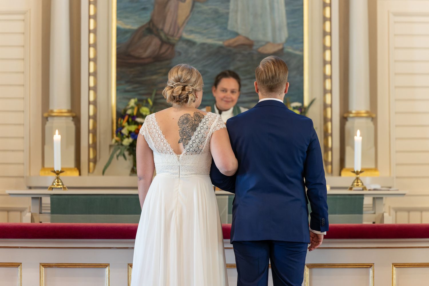 Hääpari alttarilla, taustalla vihkipastori ja alttaritaulu.
