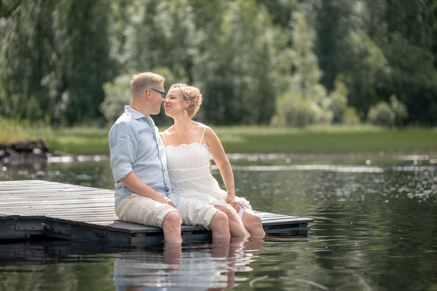 Hääpari istuu laiturilla, nenät vastakkain.