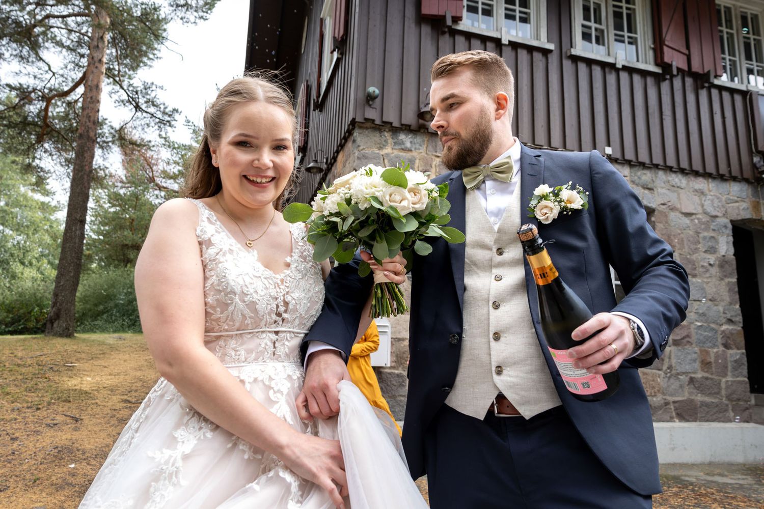Hääpari vauhdikkaana shampanjapullo kädessään.