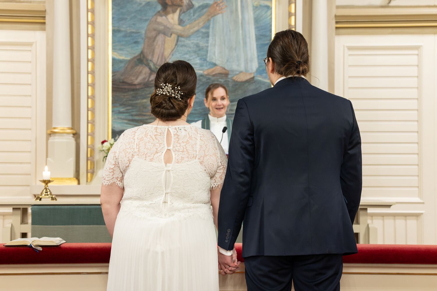 Hääpari seisoo alttarilla, heidän välistään näkyy pastori.