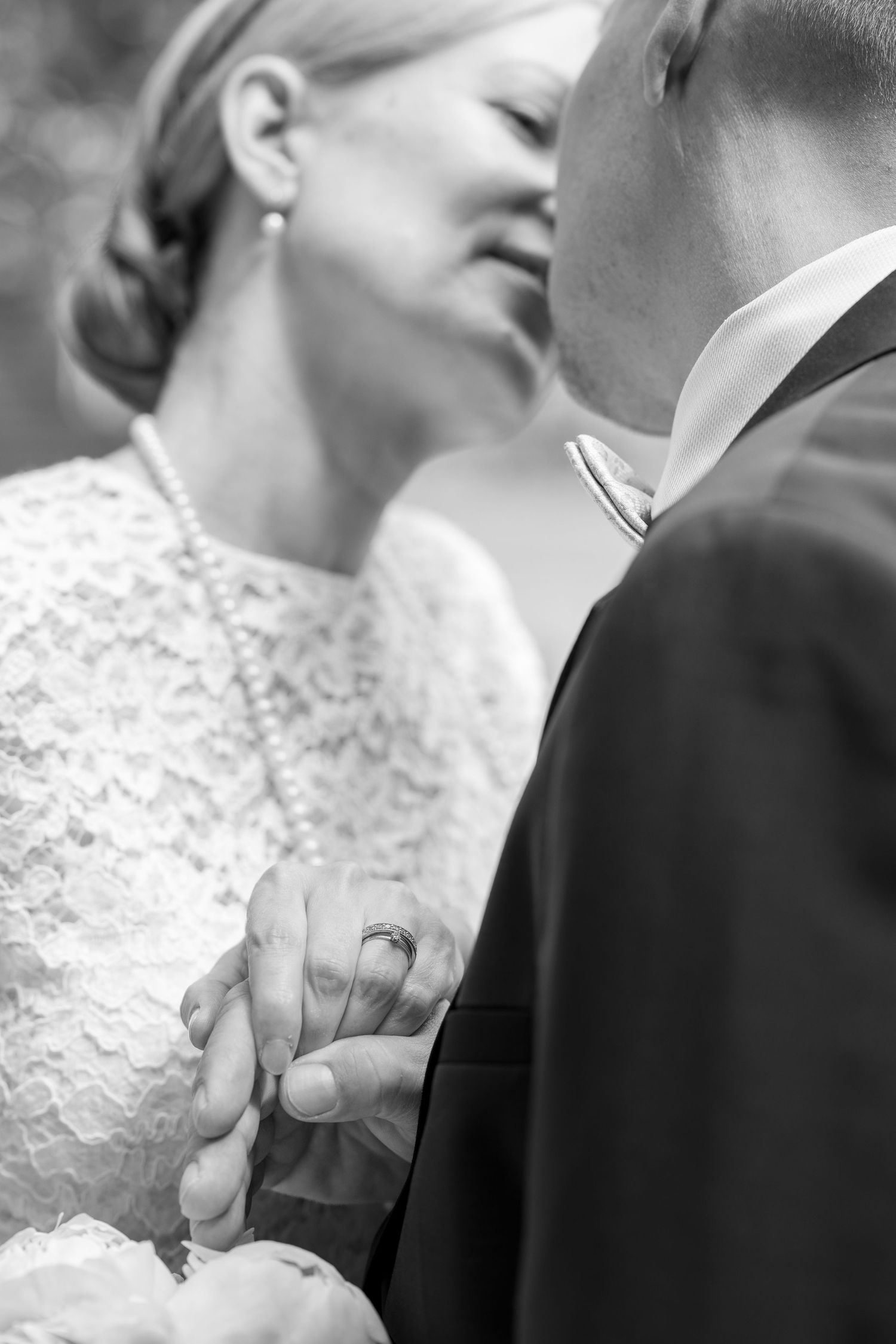 Black and white photo of bride and groom holding hands, wedding rings visible, sharing a tender moment.