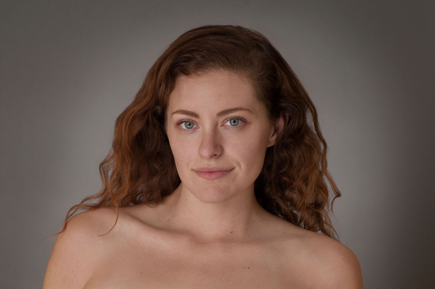 Artistic boudoir portrait against grey background showing natural beauty and confidence.