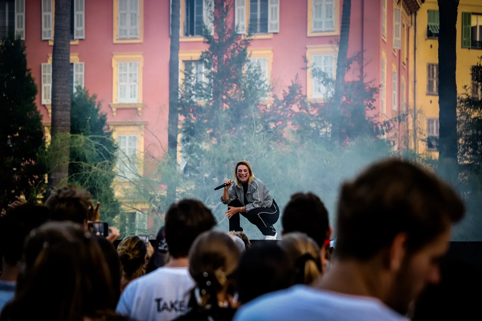 Concert en plein air en journée, un artiste joue au centre d’une scène devant une foule compacte, avec des façades colorées en arrière-plan.