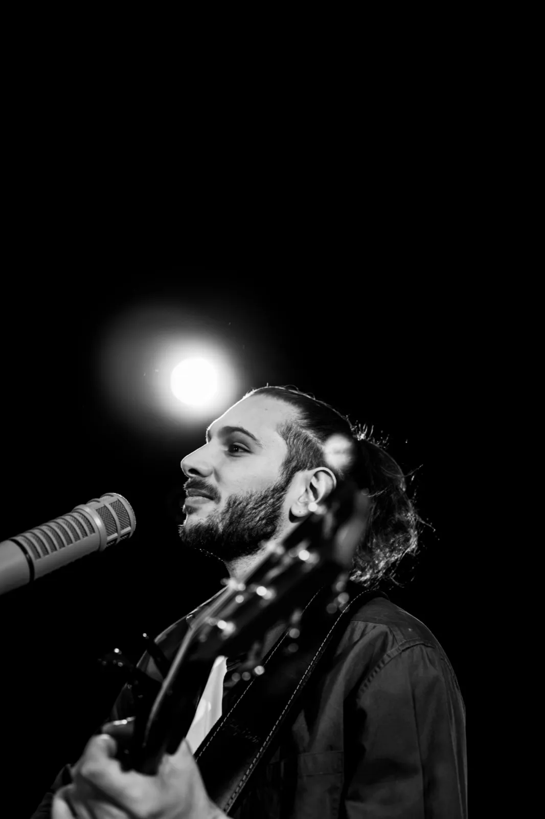Chanteur de profil en noir et blanc, micro à la bouche, avec une lumière forte formant un halo au-dessus de sa tête.