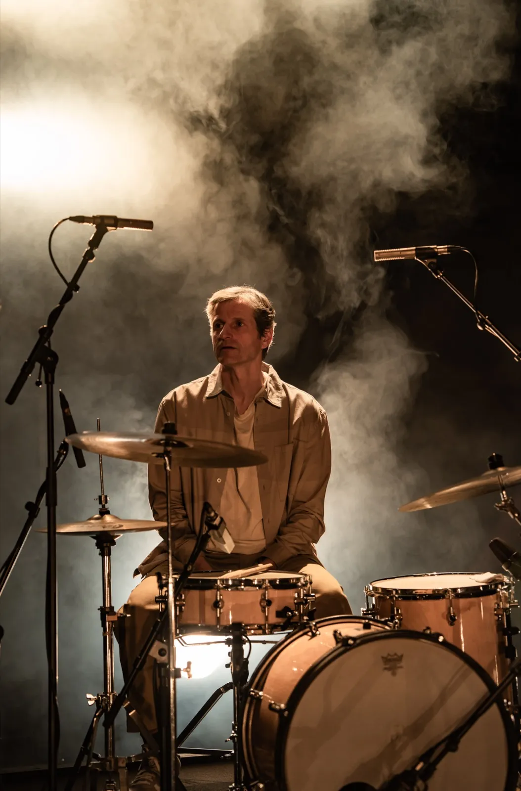 Batteur assis devant sa batterie, entouré de fumée de scène avec une lumière dramatique en contre-jour.