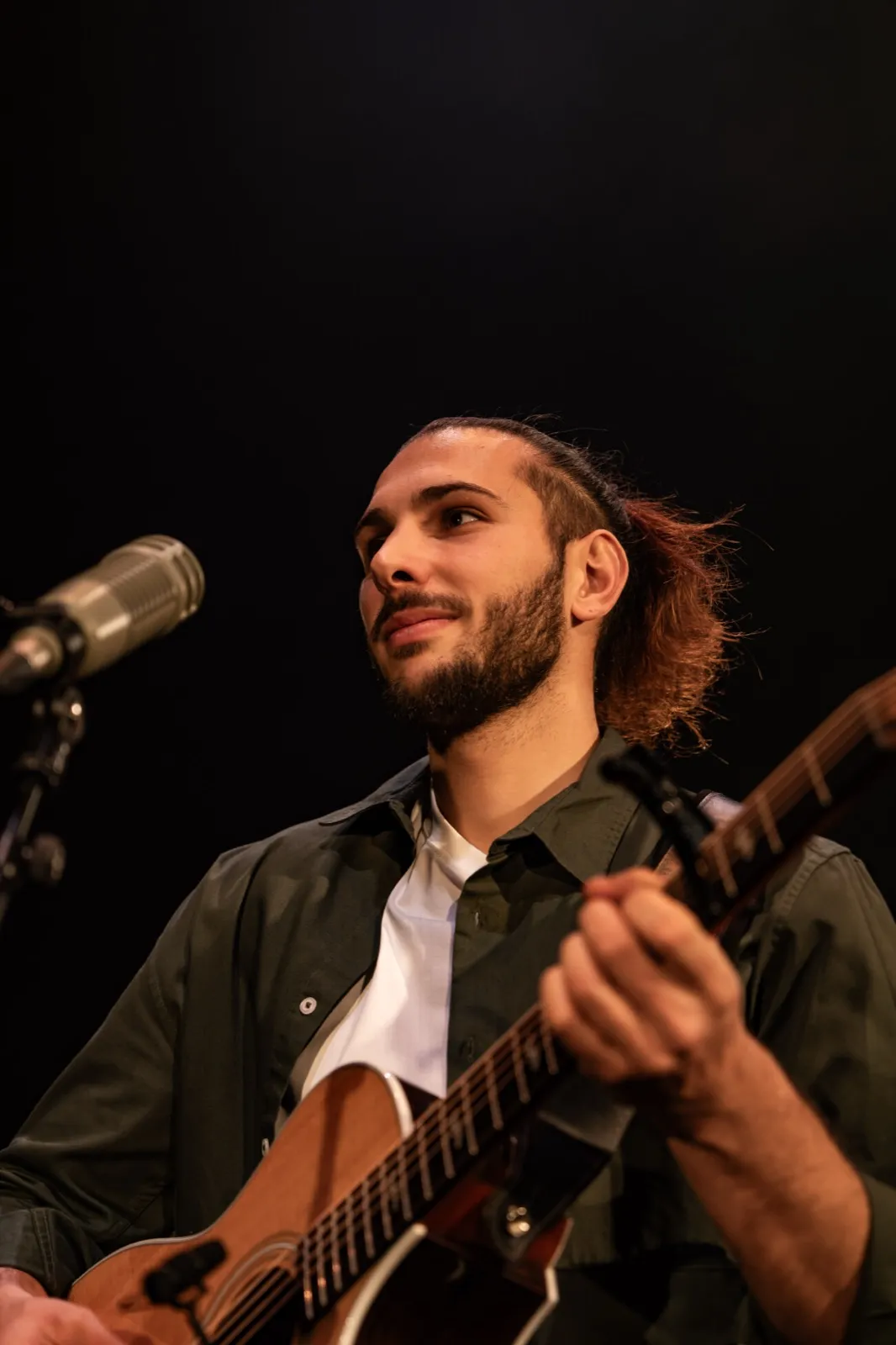 Portrait serré d’un guitariste barbu en pleine interprétation, plongé dans sa performance sous un éclairage de scène doux.