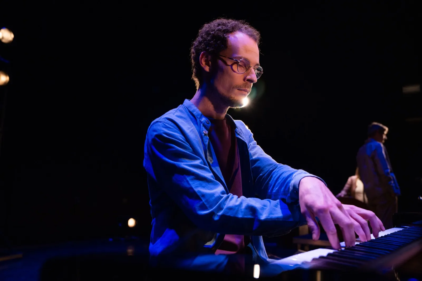 Claviériste concentré jouant sur scène sous une lumière bleue, ambiance feutrée de live.