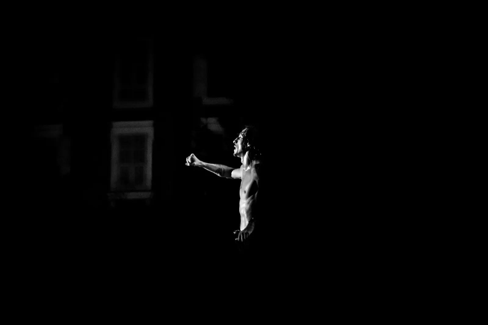 Un chanteur éclairé par un seul projecteur, debout au centre d’une scène noire, tenant un micro.