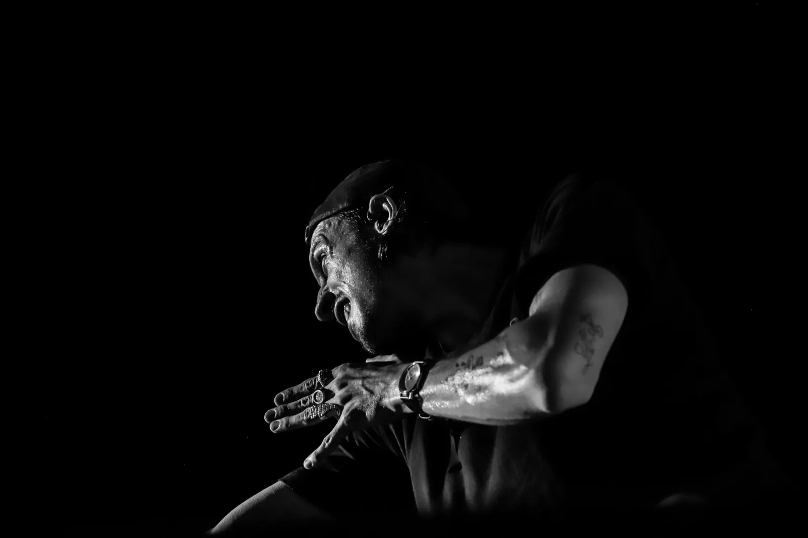 Plan rapproché d’un artiste chantant avec intensité, un bras tendu, dans une ambiance sombre et dramatique.