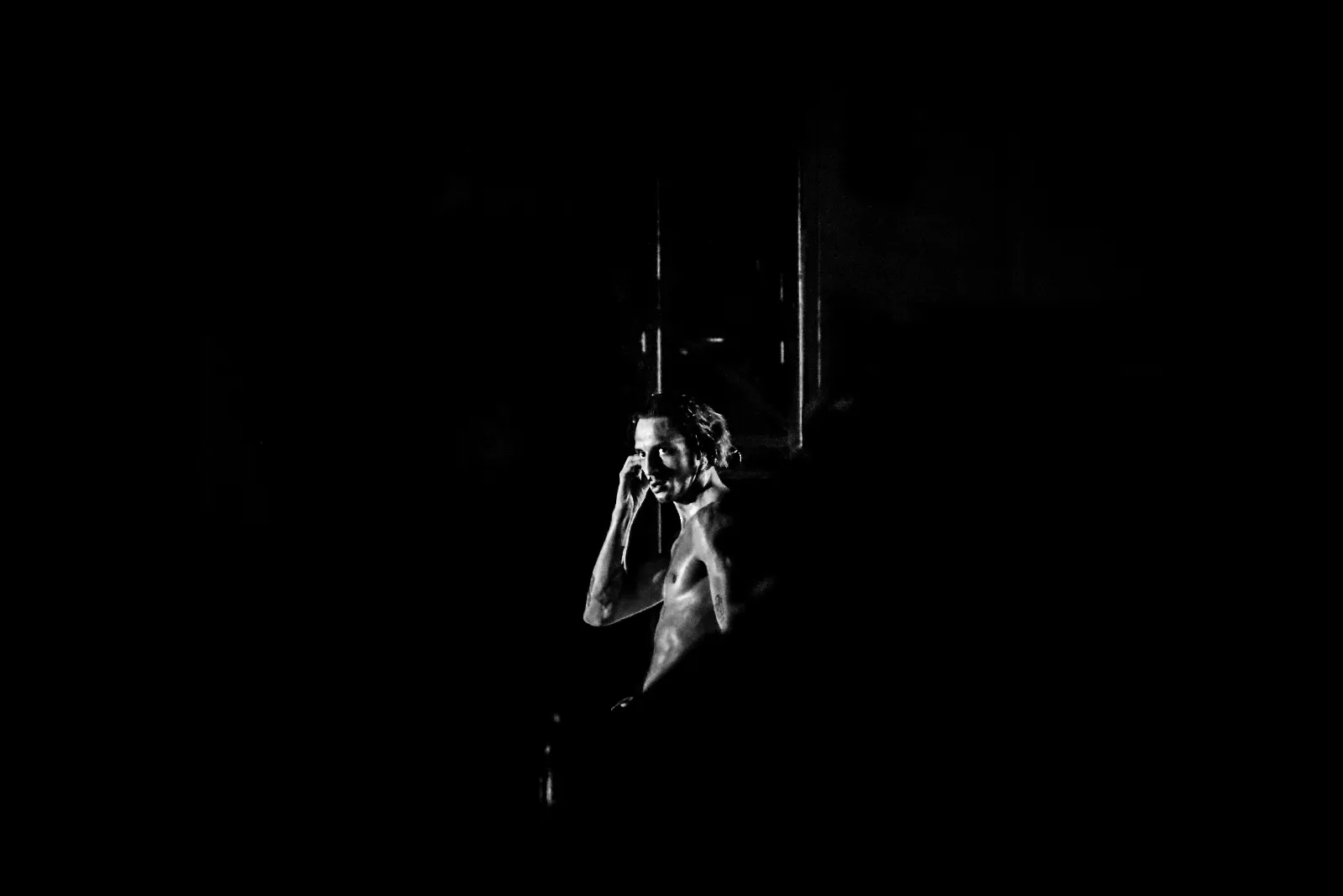 Un artiste en train de marcher ou danser, éclairé depuis le haut, créant une silhouette expressive dans l’obscurité.