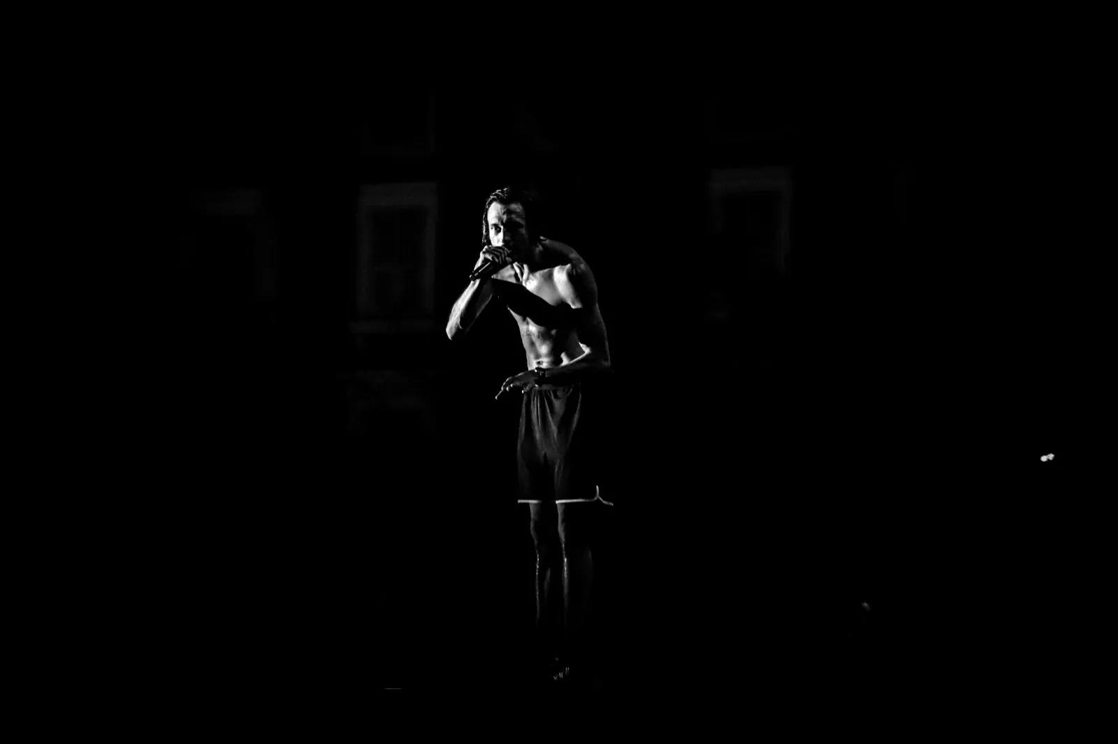 Un artiste en train de marcher ou danser, éclairé depuis le haut, créant une silhouette expressive dans l’obscurité.