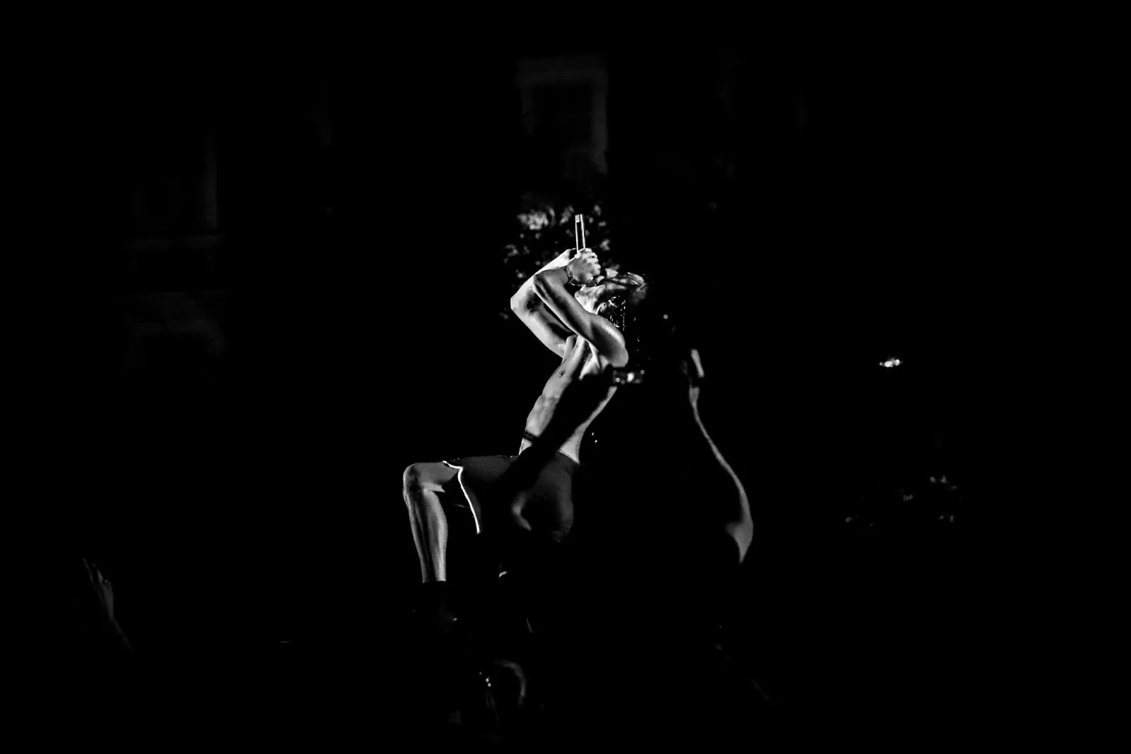 Un chanteur, éclairé par un projecteur, joue sur scène dans une atmosphère intime en noir et blanc.