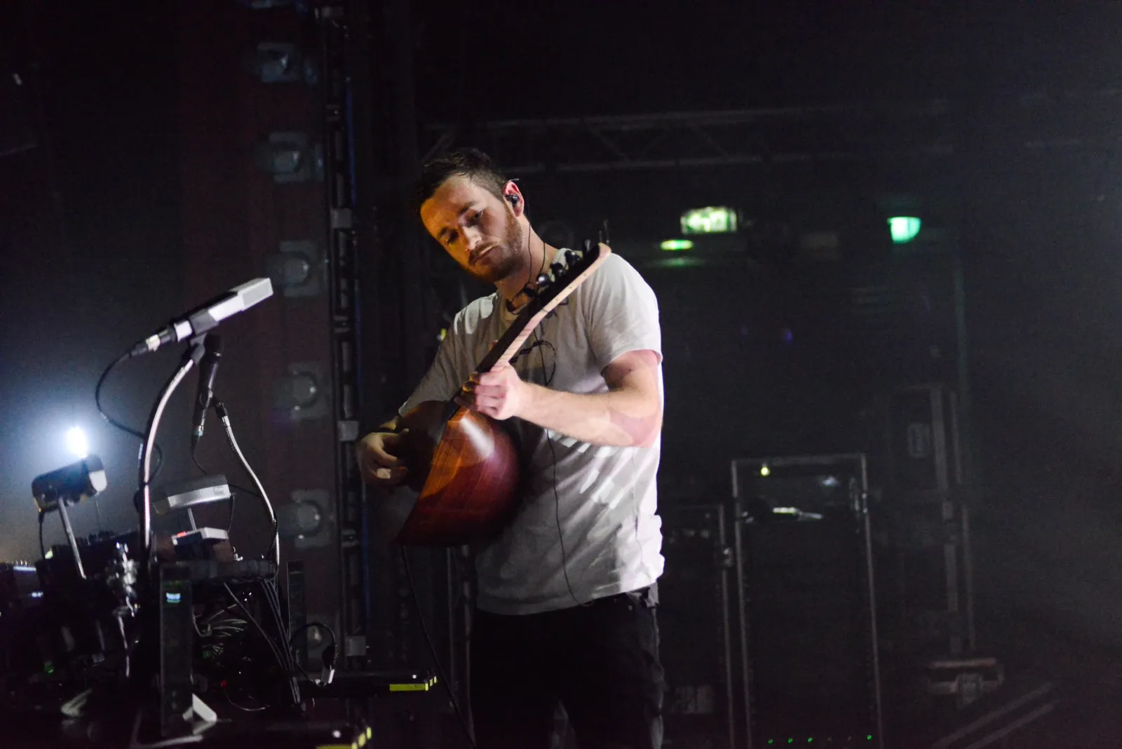 Un musicien joue de la guitare électrique sur une scène éclairée, concentré sur ses accords, avec un micro à proximité.