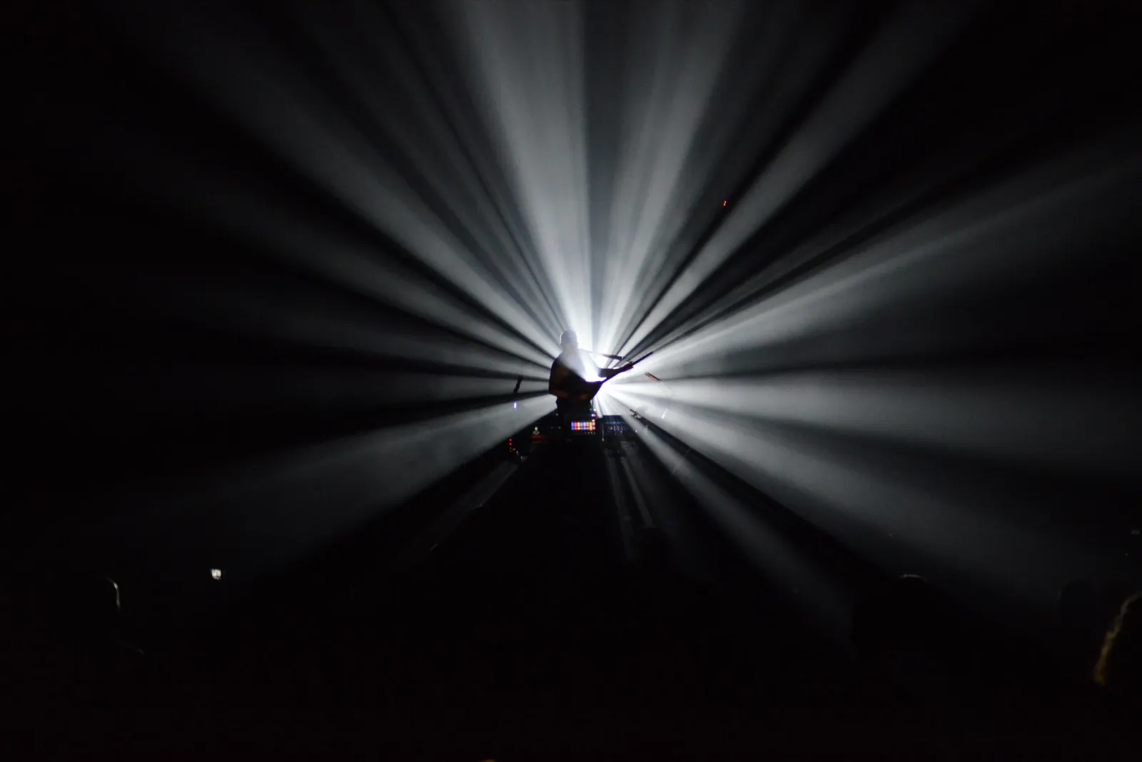 Un musicien solitaire au milieu de la scène, encadré par un faisceau radial de lumière blanche dans une ambiance dramatique.