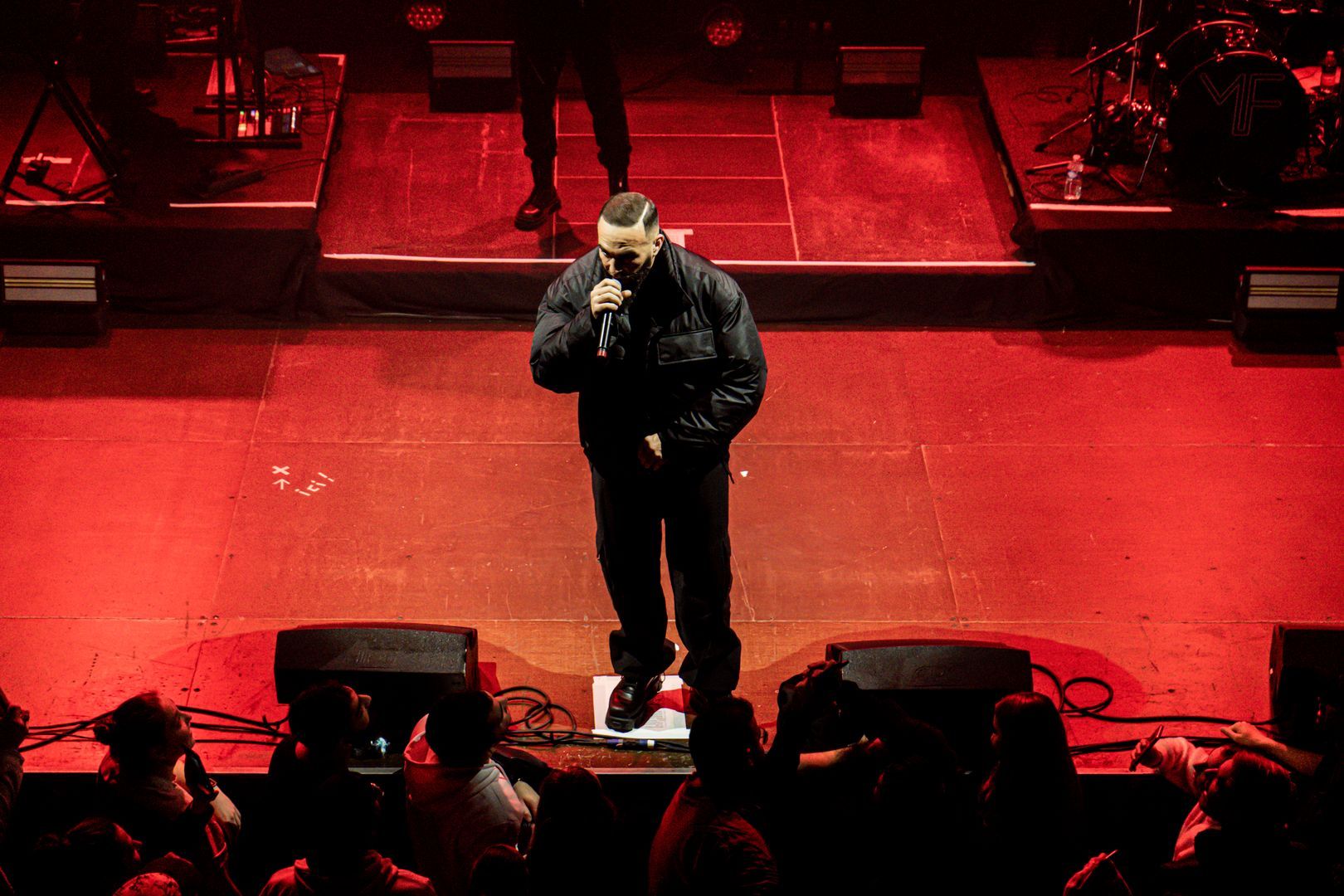 Artiste hip-hop debout au centre d’une scène rouge vif, capté en pleine performance