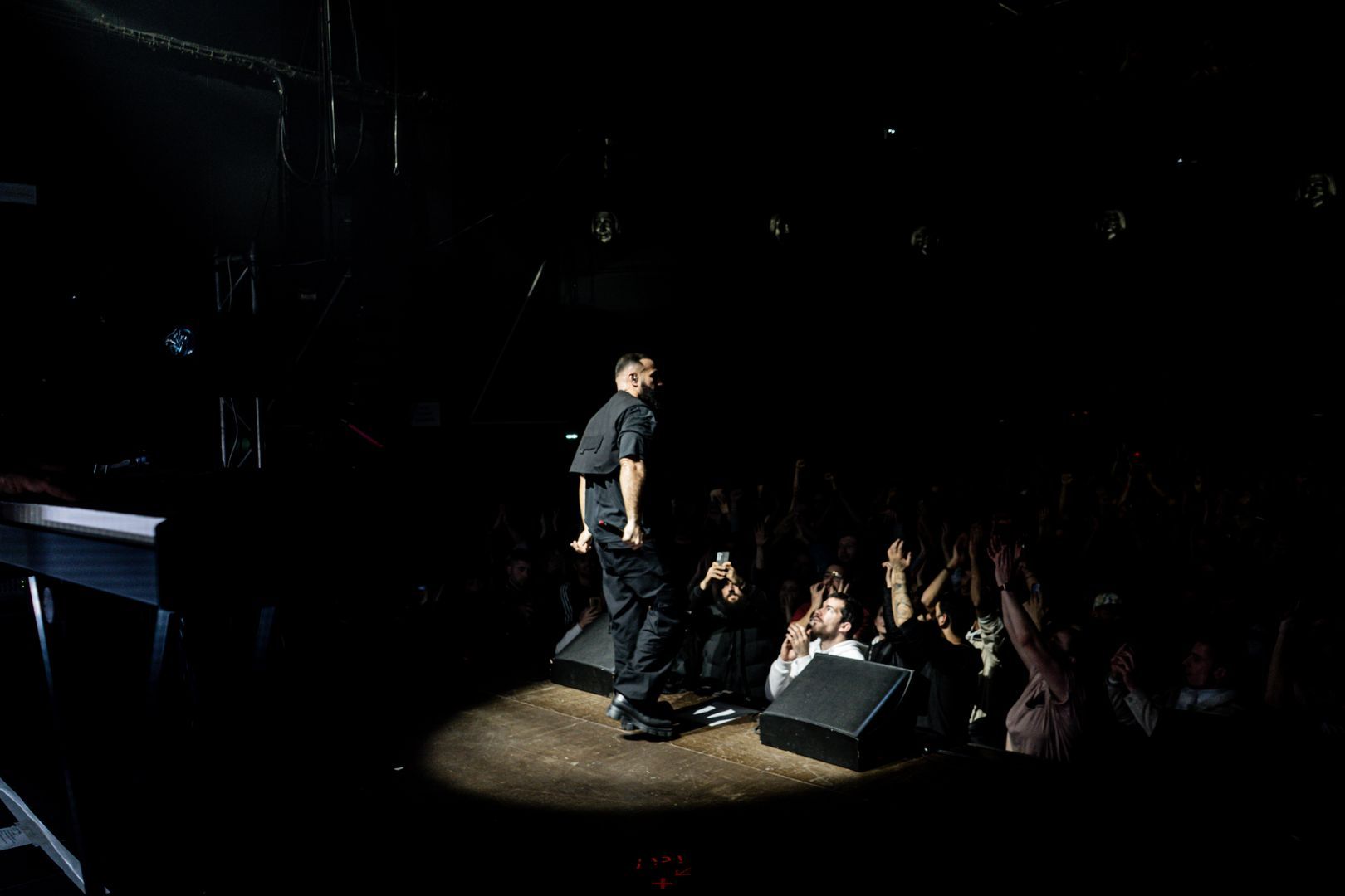Artiste hip-hop en live debout sous un projecteur, foule en interaction au premier rang