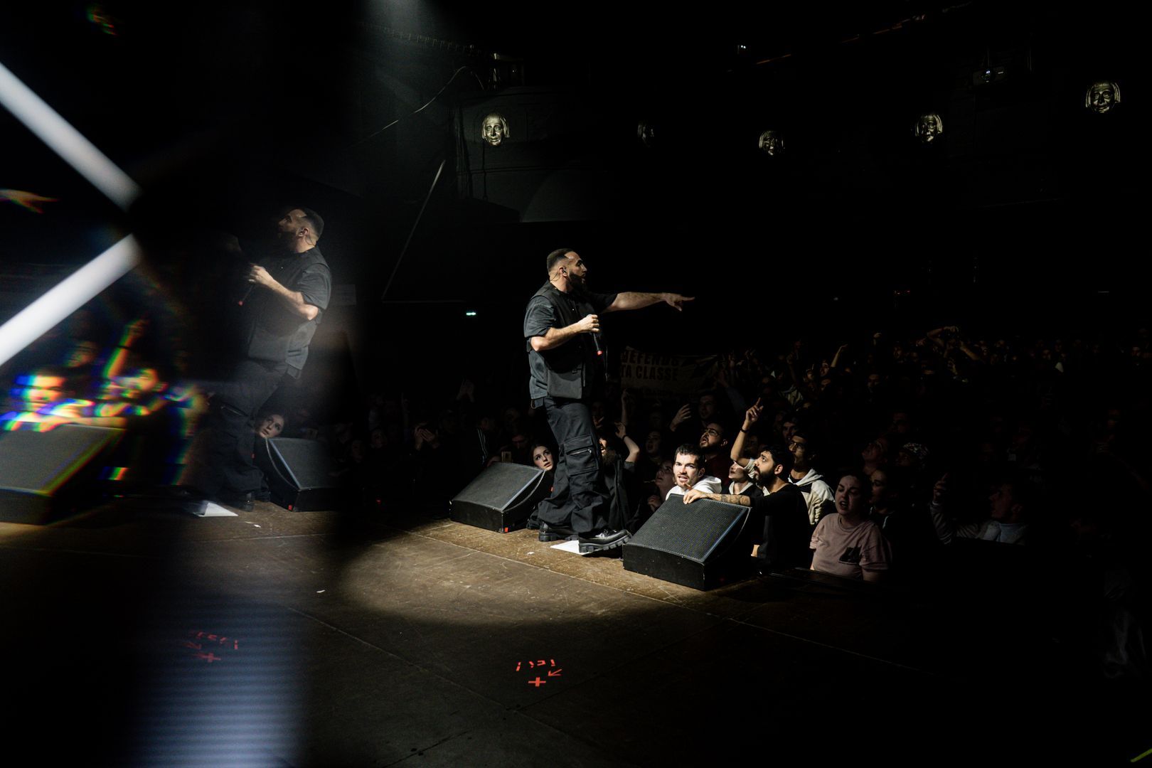 Rappeur sur scène face à un public conquis, lumière tamisée et ambiance électrique dans la salle