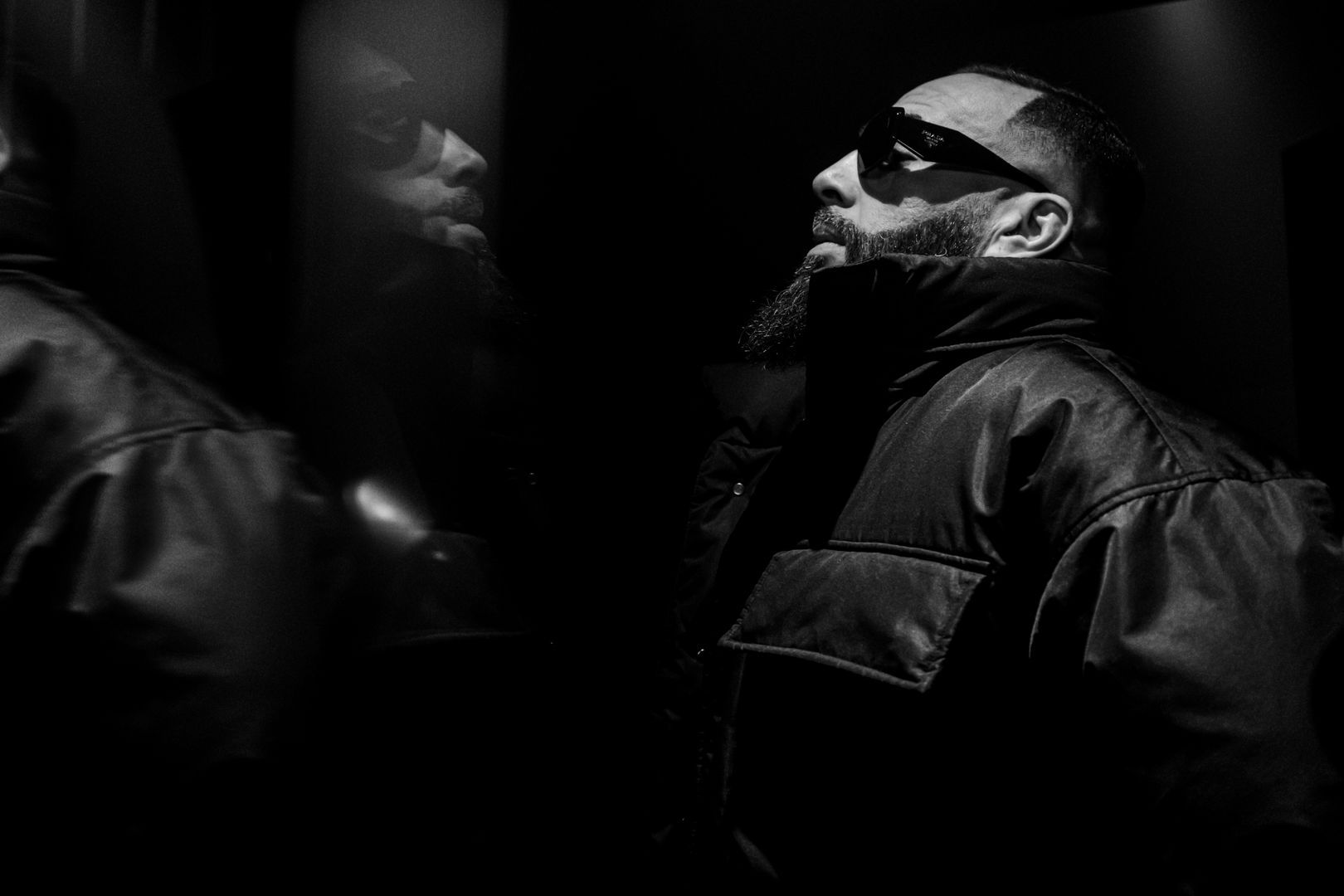 Portrait en clair-obscur d’un rappeur avec lunettes de soleil, reflet dans un miroir