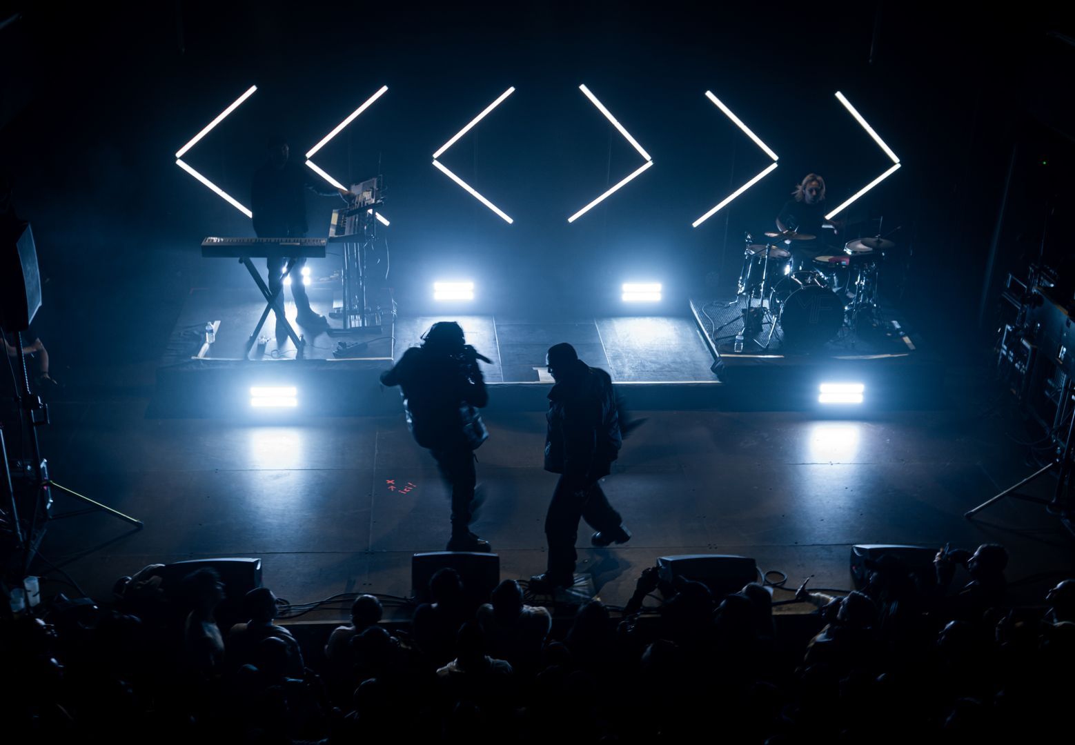 Scène de concert avec lumières LED géométriques, deux rappeurs en mouvement sur fond bleu