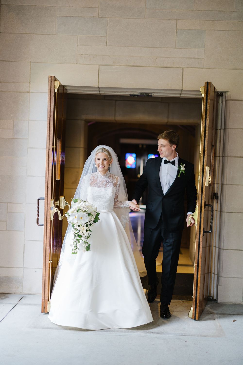 A couple walking through ornate double doors in a church building during a formal wedding ceremony.