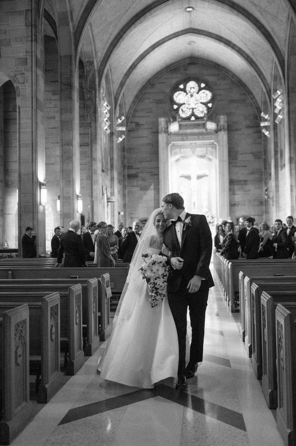 A romantic black and white wedding ceremony photo showing a couple sharing a moment in a beautiful church with vaulted ceilings.