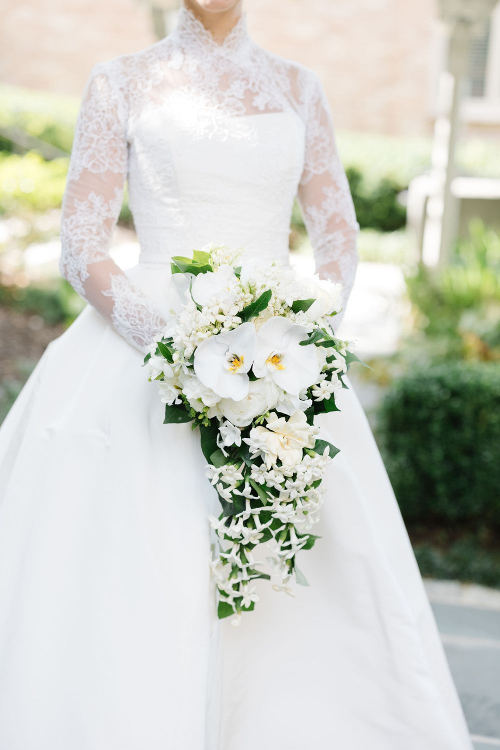 A cascading white orchid and greenery bridal bouquet paired with an elegant lace-sleeved wedding gown.