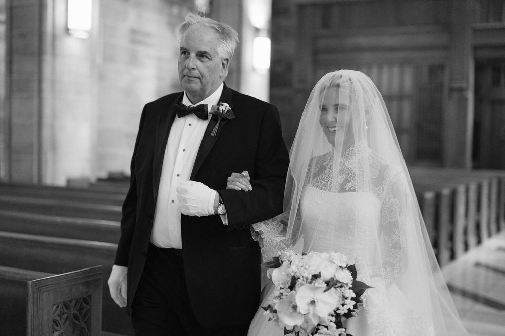 A black and white photograph of a traditional church wedding moment with a bride in a veil holding a floral bouquet.