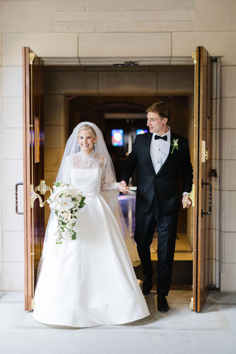 A couple steps through ornate church doors on their wedding day, with the bride wearing a classic white gown and flowing veil.