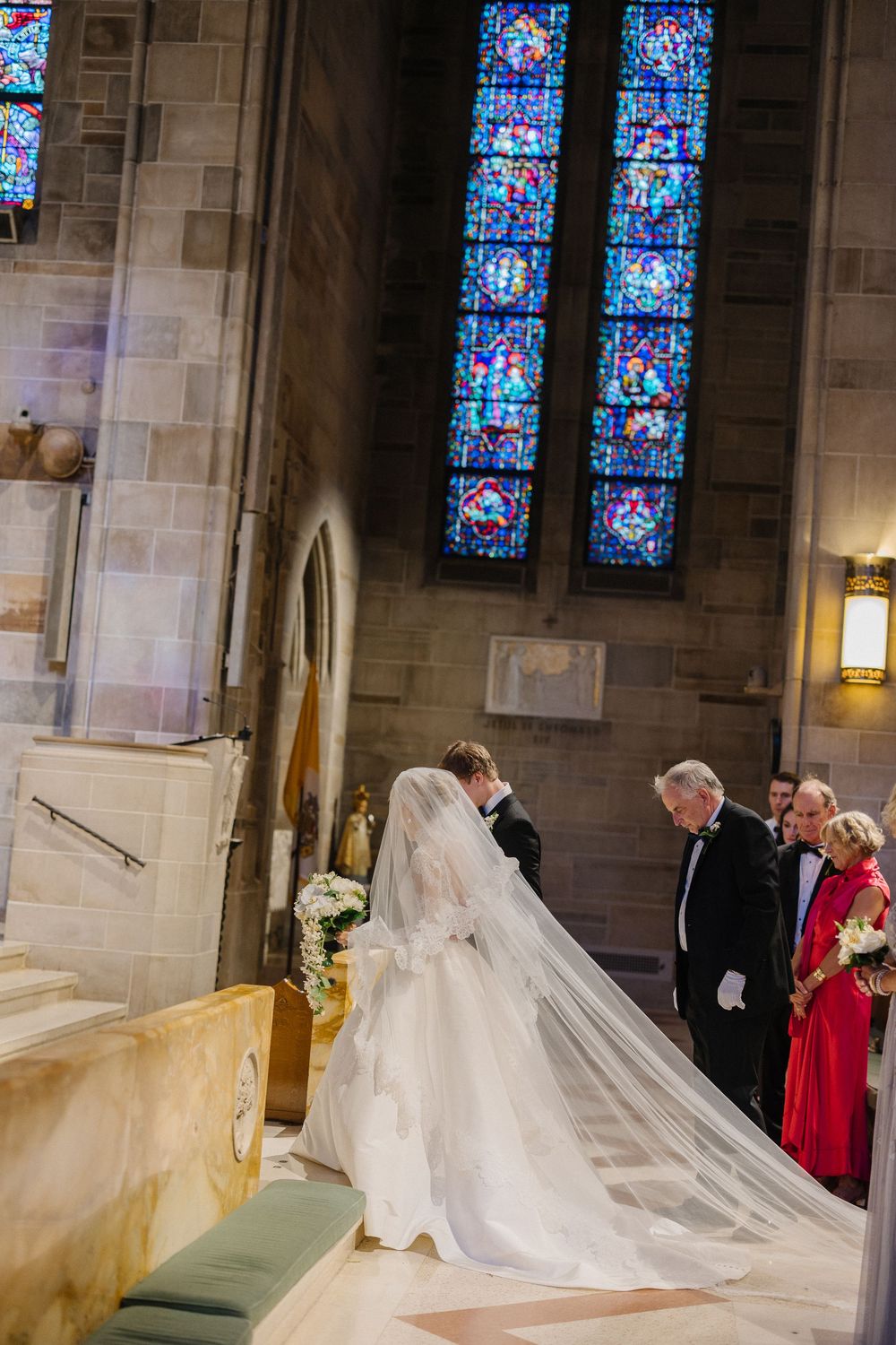 A traditional church wedding ceremony takes place beneath beautiful stained glass windows in a stone cathedral.