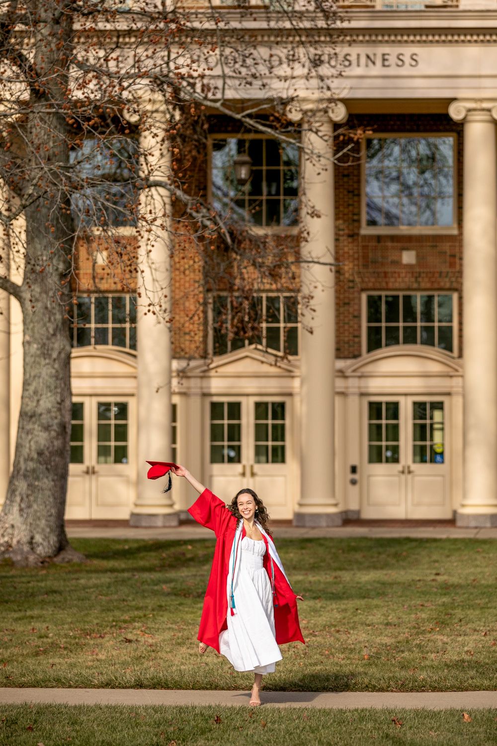 Graduate in red cap and gown celebrates in front of ornate academic building with classical columns.