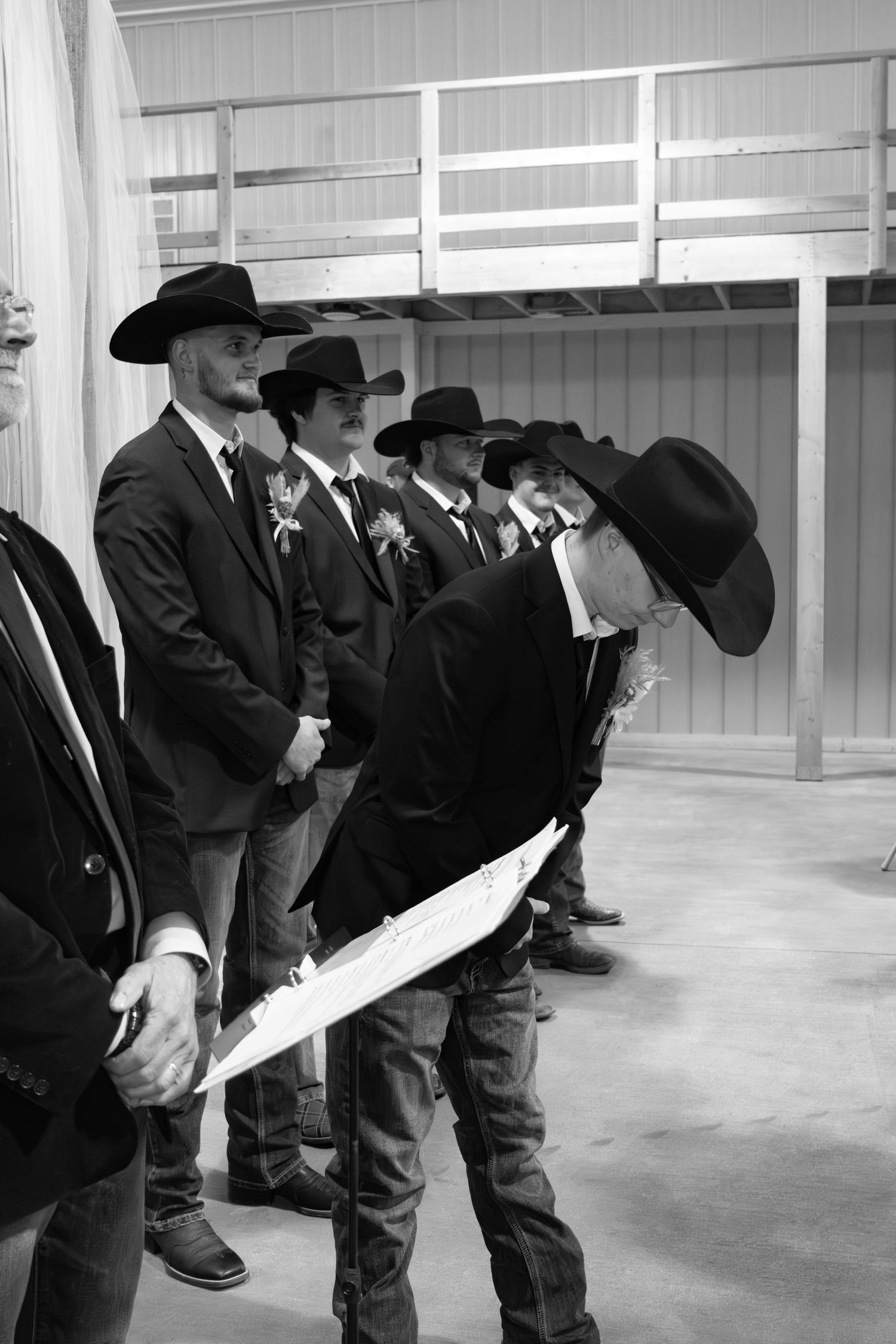 A line of cowboys in Western attire with black cowboy hats standing together in a covered arena.