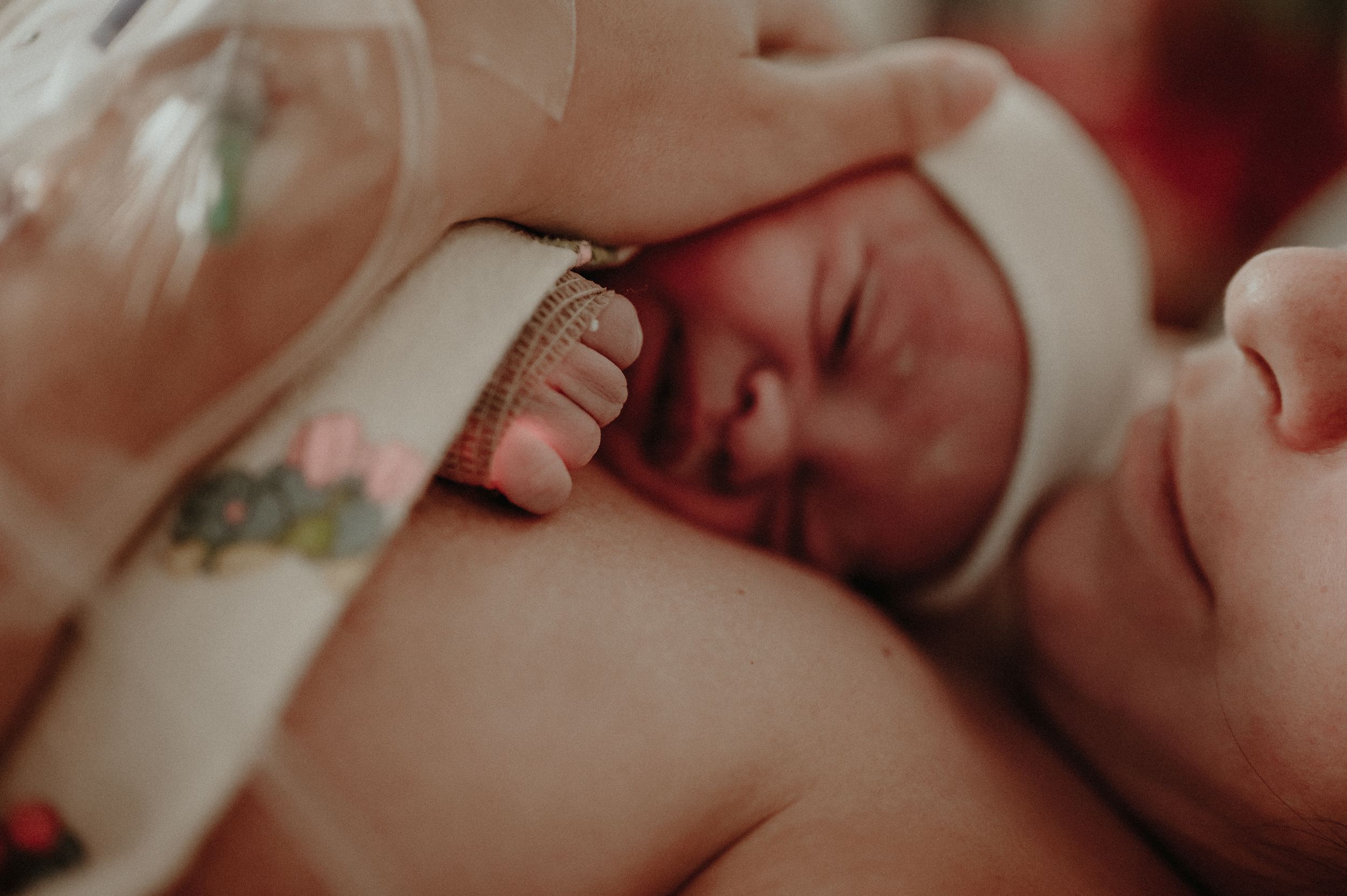 A newborn baby rests peacefully on a soft white blanket in warm lighting.
