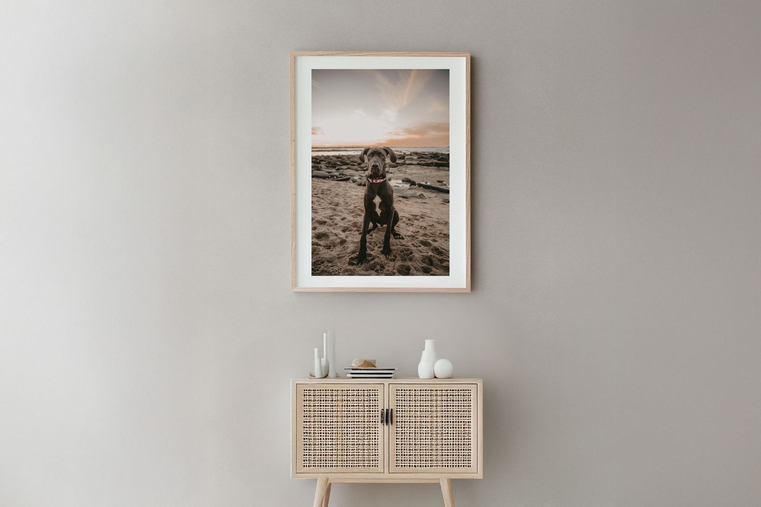 A framed black and white photograph of a silhouette on a beach hangs above a modern rattan cabinet with decor.