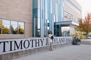 Modern building exterior with stone signage reading 'Timothy J. Hyland Hall' and reflective glass windows on a sunny autumn day.