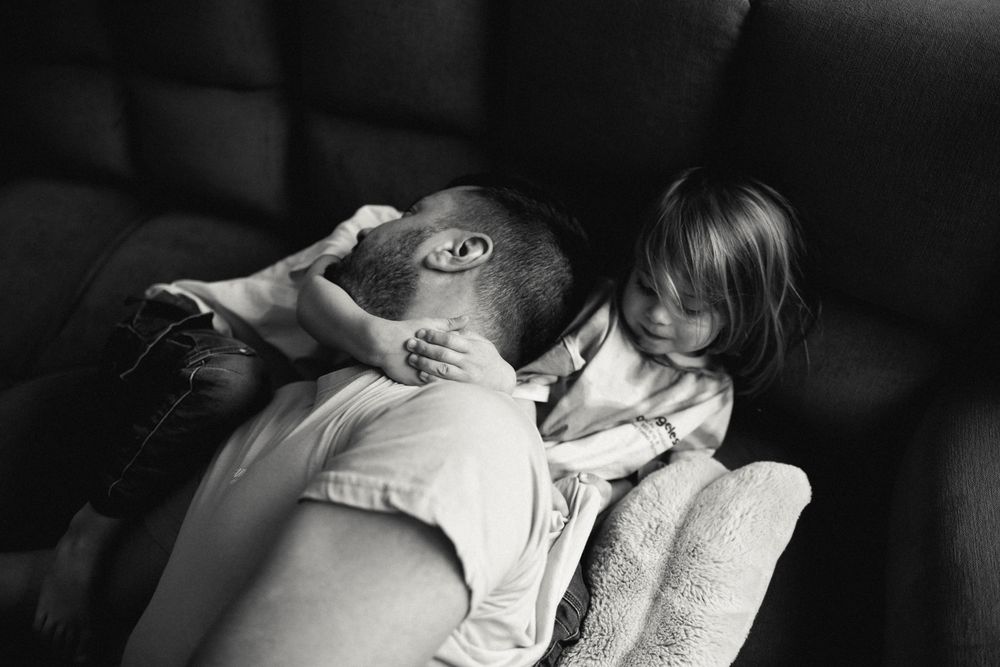 Black and white photo showing a tender moment between two people in an intimate embrace on a chair.