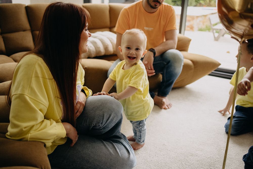 Family in matching yellow outfits sits together on beige carpet and couch during relaxed indoor gathering.