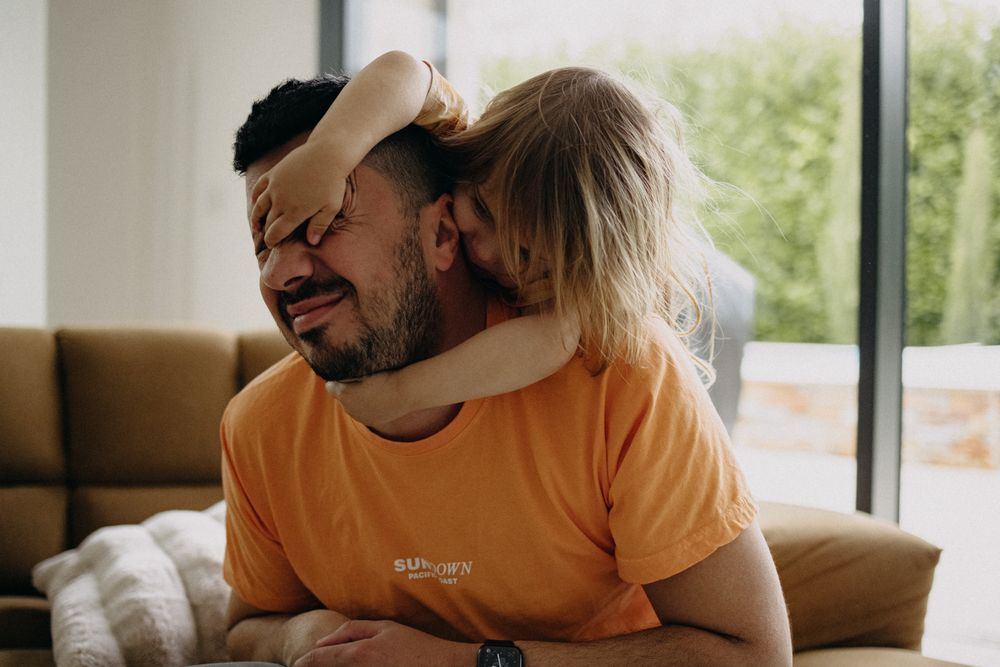 A sweet moment of affection shared between two people on a tan couch in a bright room.